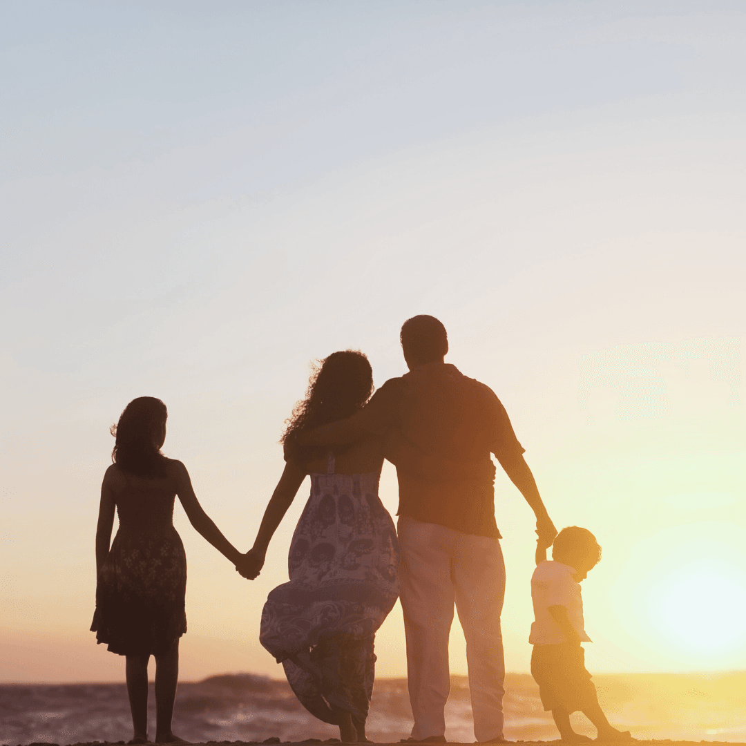 Silhouetted family of four stands on a beach, holding hands and facing the sunset, symbolizing life transformation as they embrace new beginnings together.